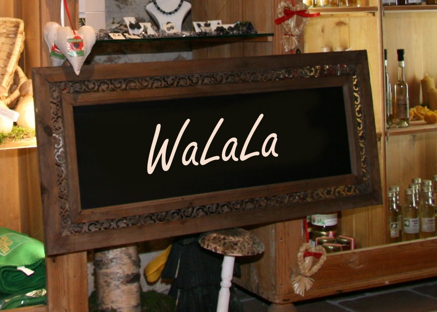 A decorative wooden sign with the inscription 'WaLaLa' in a rustic store with shelves full of products.