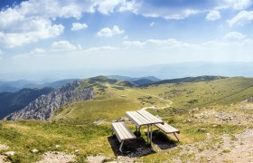 Panoramic view from a mountain with a bench in the foreground and green hills in the background.
