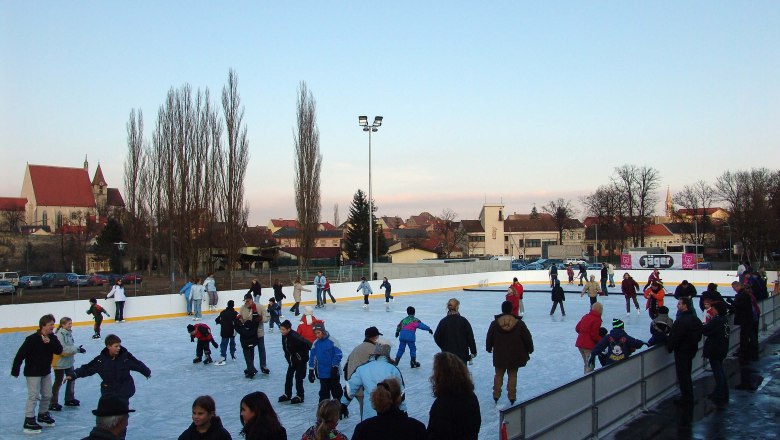 People skating on an open-air ice rink with a church in the background.