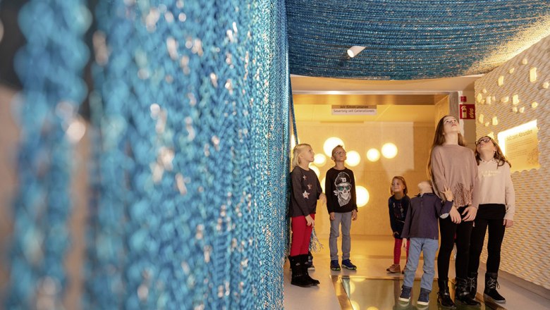 Children stand in a room with blue, hanging nets and illuminated walls.