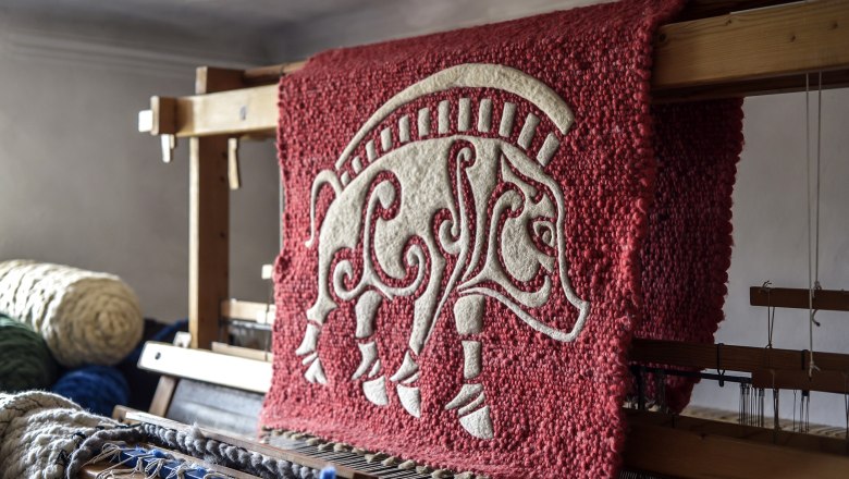 A red tapestry with a white, stylized animal motif on a loom.