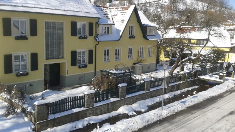Pension Hendling, © Josef Hendling Yellow house covered with snow in winter, surrounded by a fence and trees.