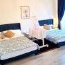 One bedroom with two double beds, a baby crib in the middle and blue curtains.