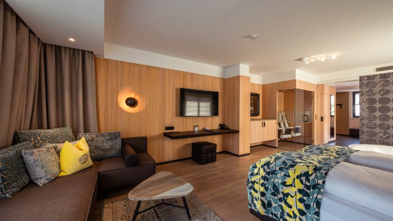 Modern hotel room with wood paneling, sofa, bed and flat-screen TV.