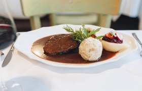 A plate with saddle of venison, bread dumplings, pear with cranberries and sauce, decorated with herbs.