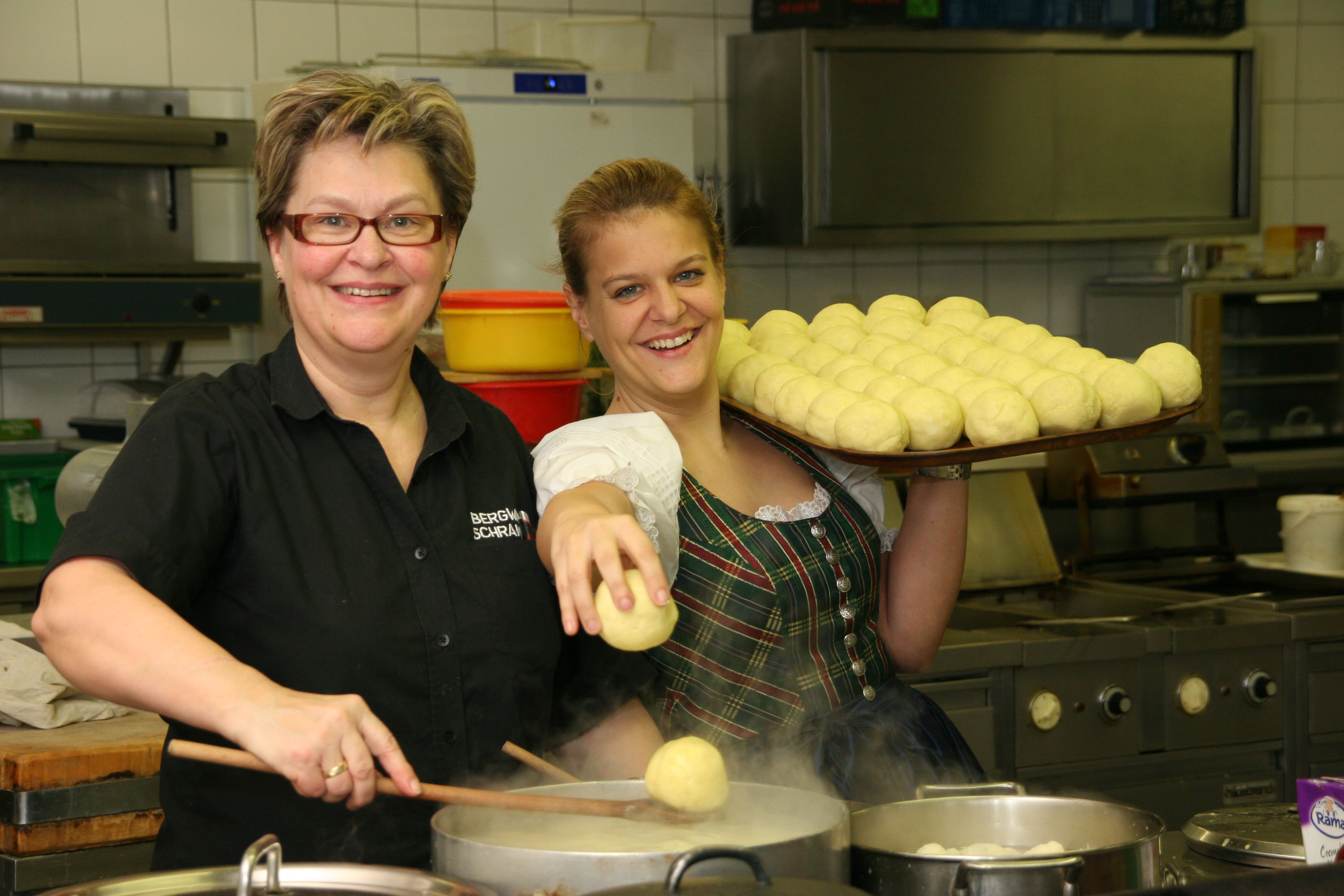 Two women in a kitchen, one holding a tray of dumplings, the other cooking dumplings in a pot.