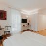 Modern, bright hotel room with double bed, TV, table and chairs, wardrobe and decorative picture on the wall.
