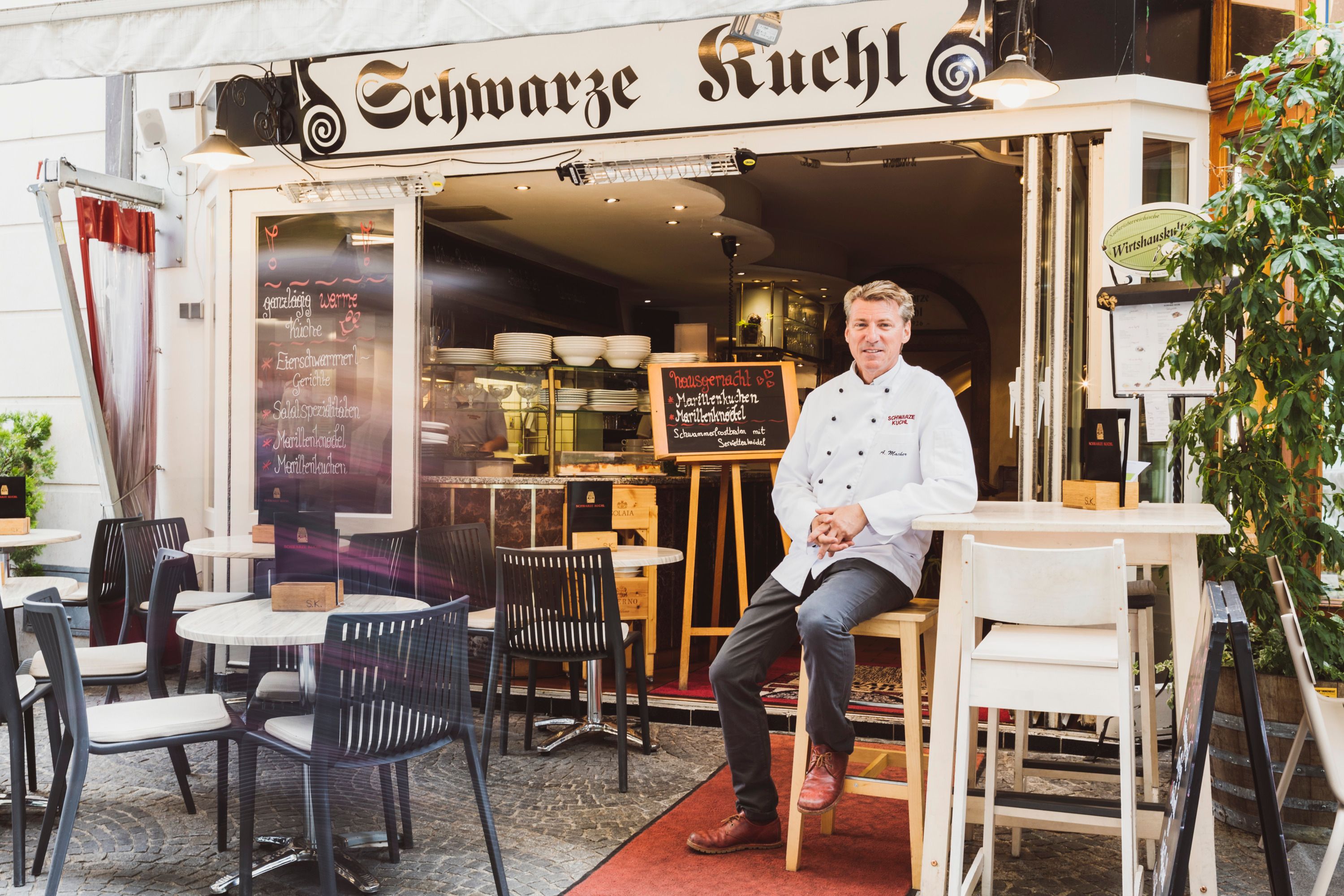 Restaurant 'Schwarze Kuchl' with chef in front of the entrance, tables outside.