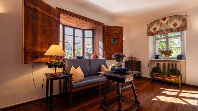 Cozy living room with wooden floor, sofa, table and lamp in front of a large window with wooden shutters.