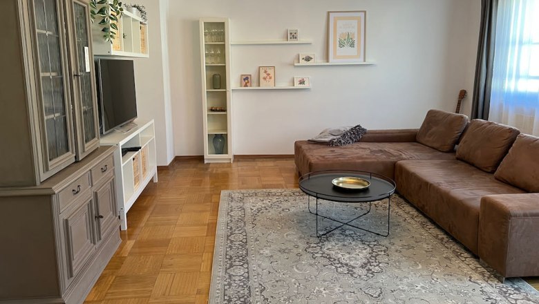 Living room with brown sofa, carpet, chandelier and TV cabinet.