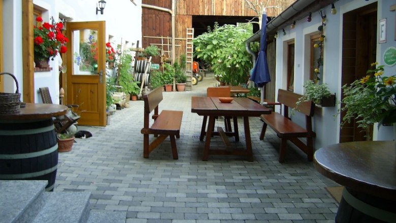 Radlerhof Kienesberger, © Kienesberger Inner courtyard of a farm with wooden tables and benches, surrounded by plants and flowers.
