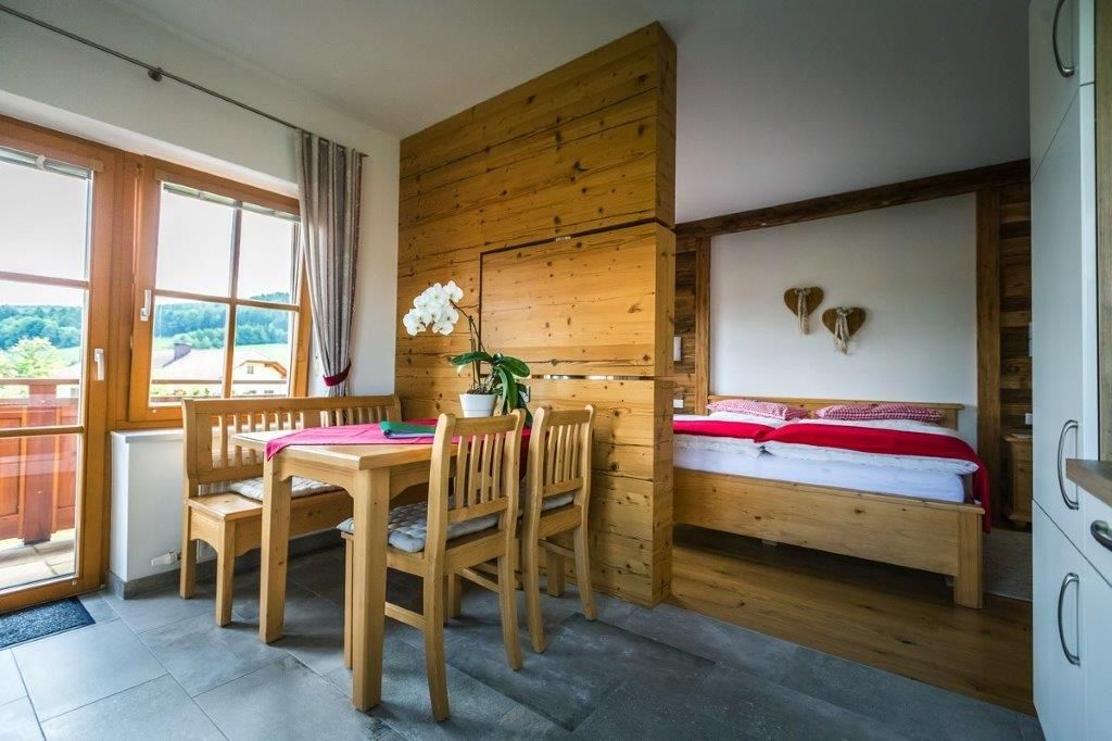 Cozy room with wooden furniture, dining table, chairs and a bed. Window with a view of the green landscape.