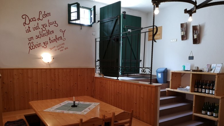 Interior view of a cozy wine cellar with wooden tables and shelves, decorated with a Goethe quote on the wall.