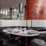 Modern restaurant with a table setting, black leather seats and large red columns.