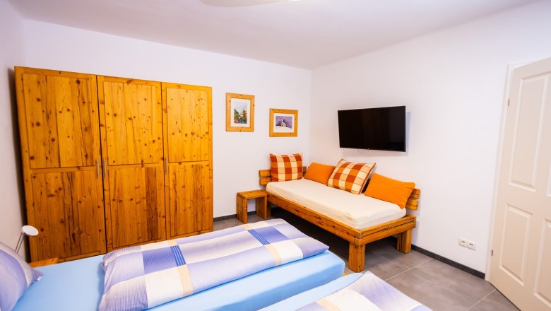 Bedroom with wooden furniture, two beds, sofa, wardrobe, TV and pictures on the wall.