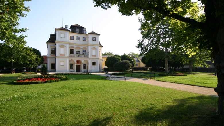 The Belvedereschlössl in Stockerau, surrounded by a well-tended garden with trees and flowerbeds.