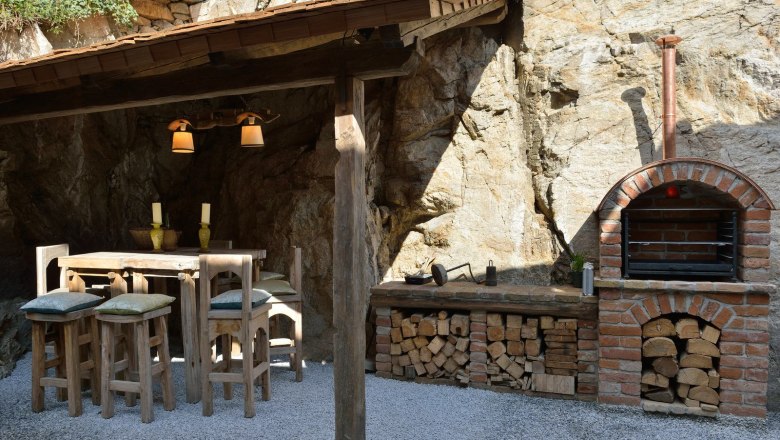 Rustic outdoor area with wooden table, chairs and brick oven.