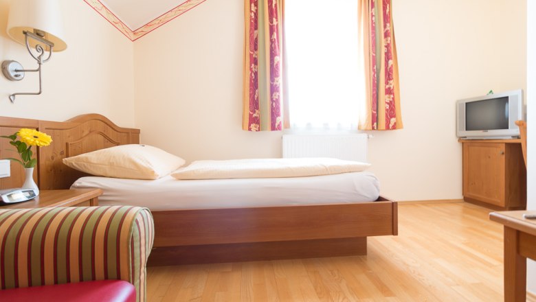 Single room with bed, TV and armchair.