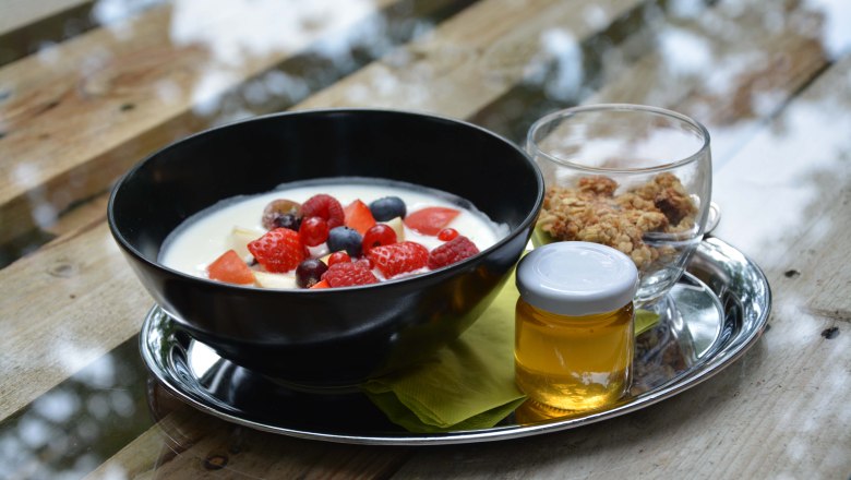 Black bowl with yogurt and berries on a silver tray with honey and muesli.