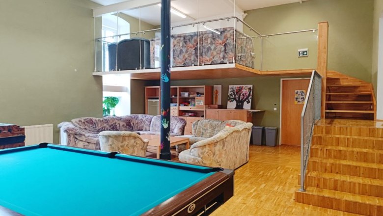 A youth room with a pool table, sofas and a gallery with stairs.
