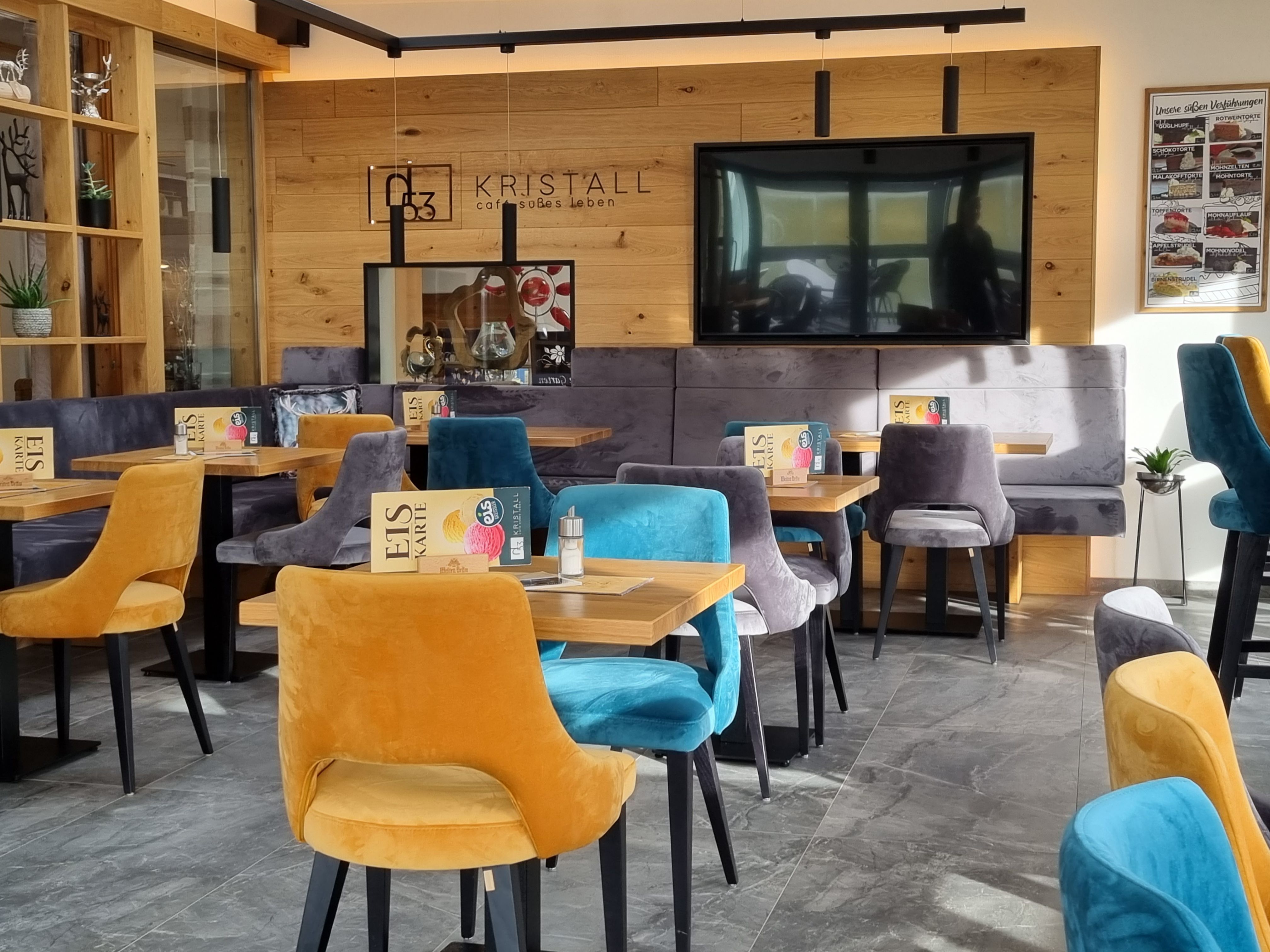 Interior view of a modern café with colorful velvet chairs and wooden walls.