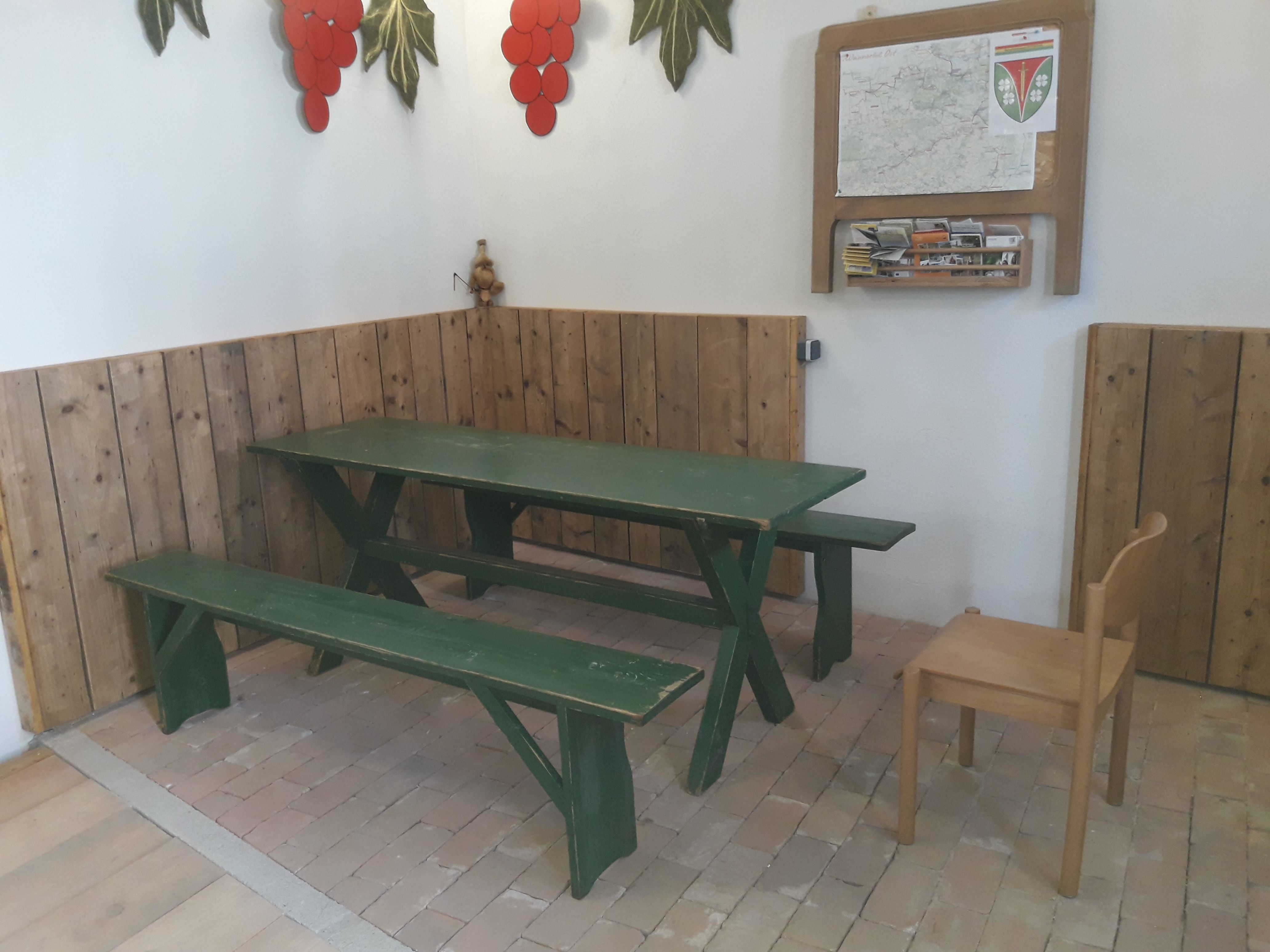 A rustic room with a green wooden table and benches, decorated with grape motifs on the wall.
