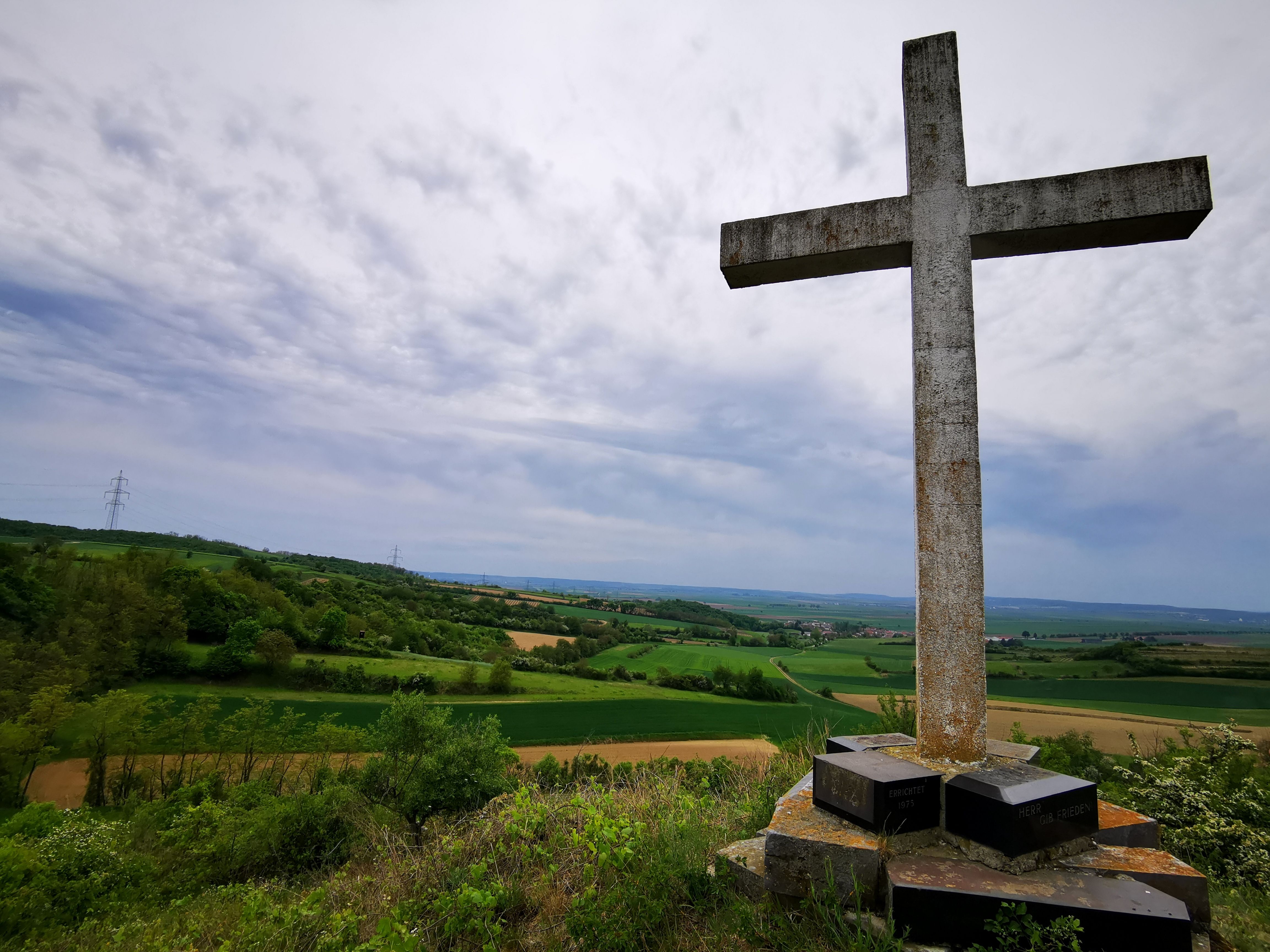 A large stone cross on a hill overlooking a green landscape and cloudy sky.