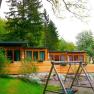 A country inn with a wooden façade and playground in the foreground, surrounded by trees.