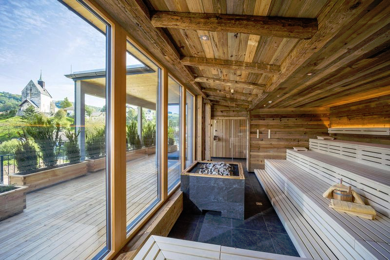 Modern sauna with wood paneling, dark tiles and glass front with a view of the outdoors.