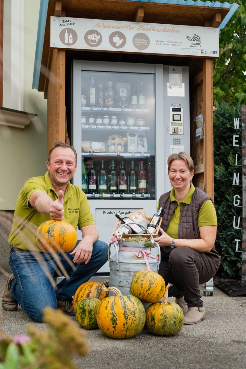 Two people in front of a self-service vending machine with pumpkins and regional products.