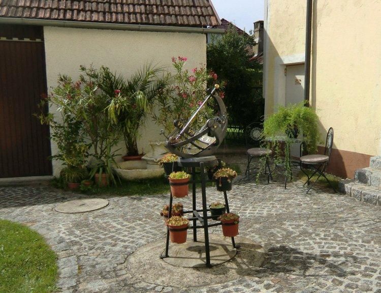 A sunny courtyard with sundial, plants and garden furniture.