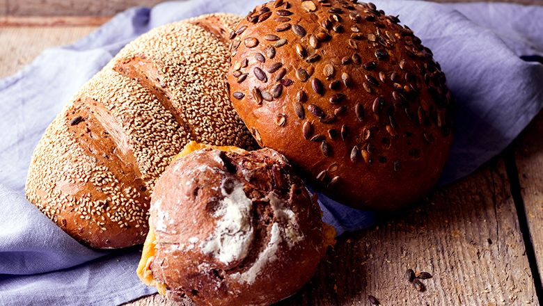 Three different breads on a blue cloth, two of them sprinkled with grains.