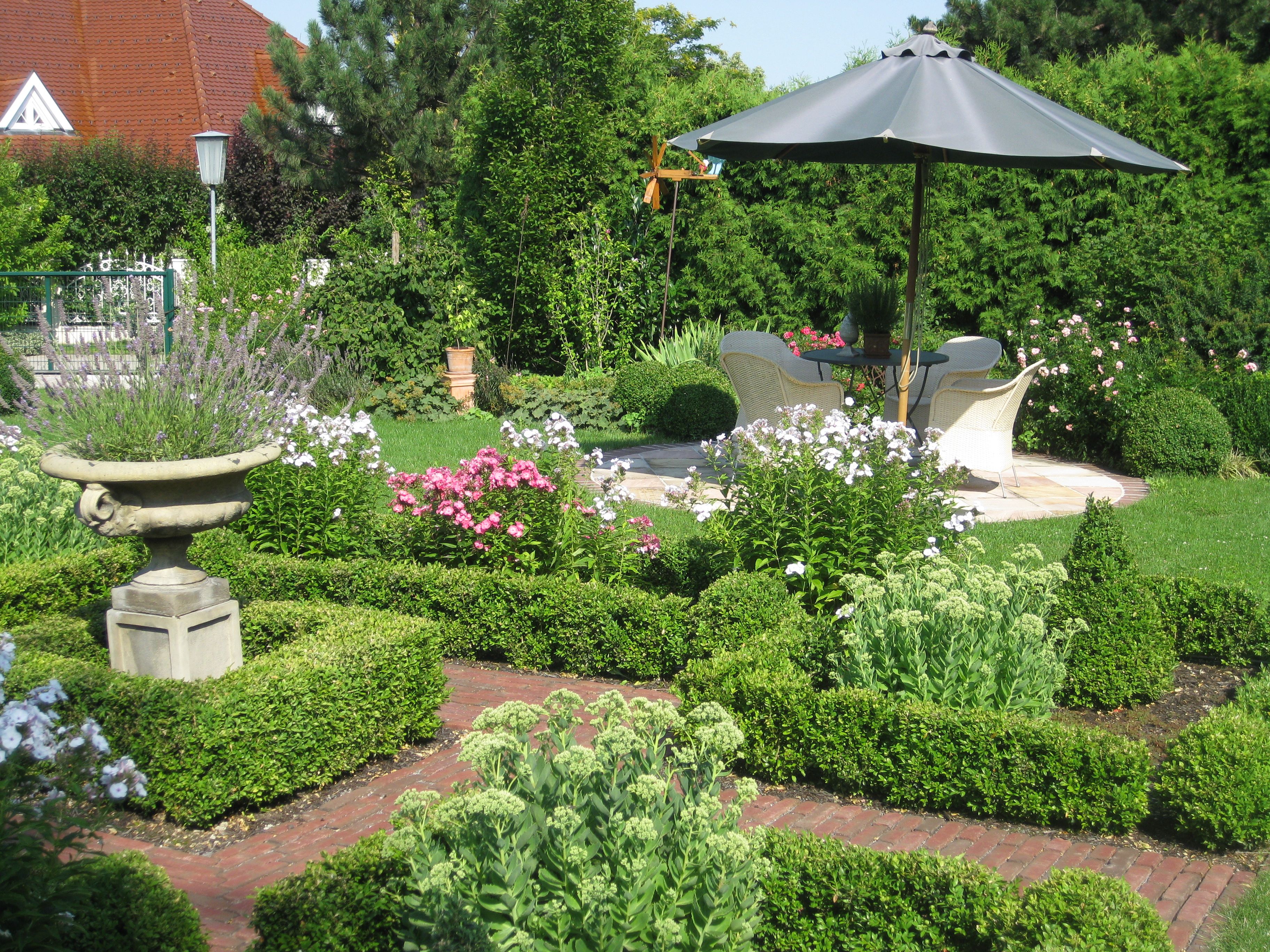 A well-tended garden with flower beds, a parasol and seating area.