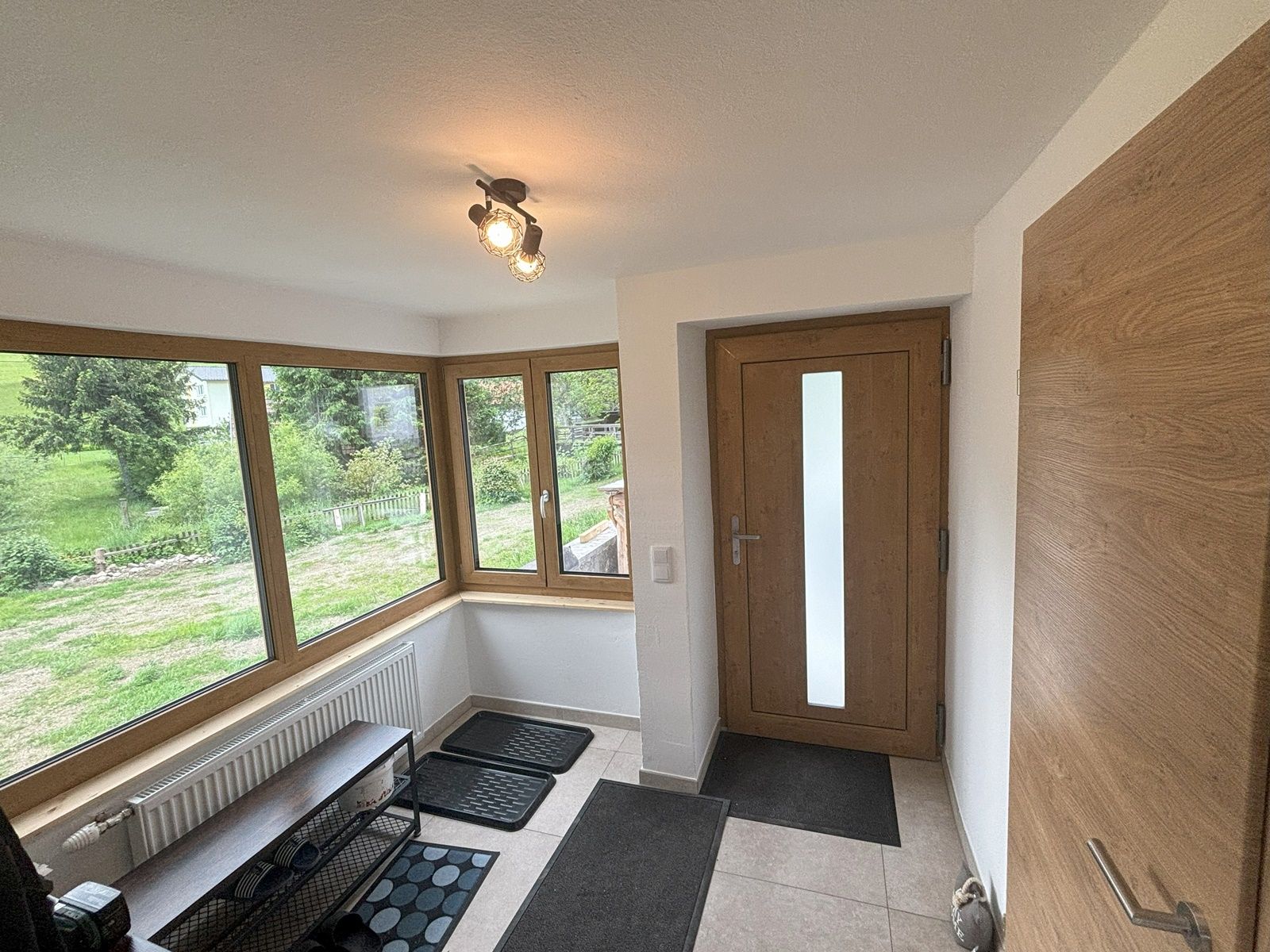 Bright entrance hall with large windows, wooden door and tiled floor.