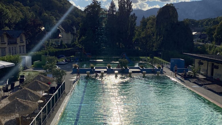 An outdoor pool with clear water, surrounded by trees and mountains in the background.