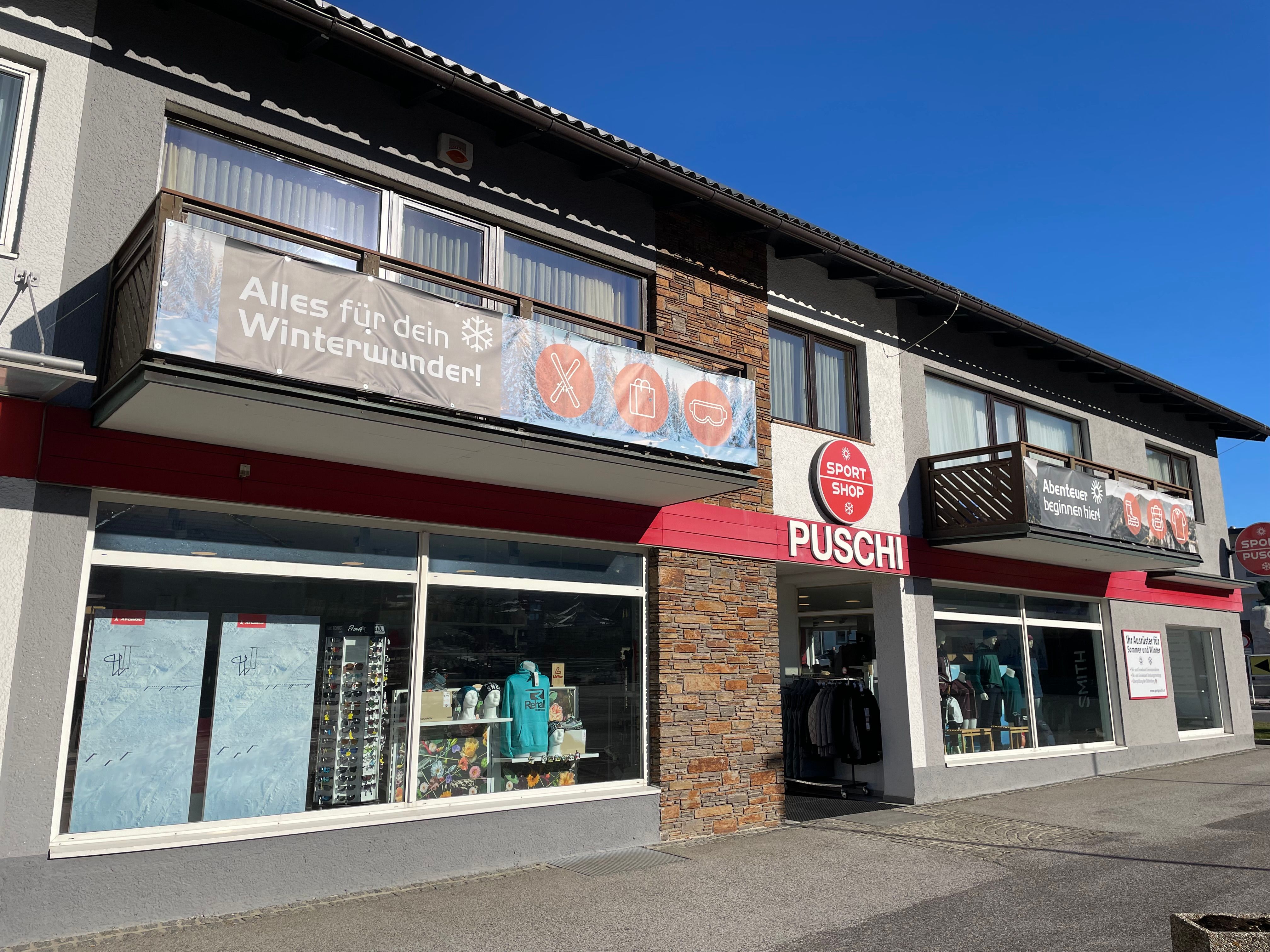 Exterior view of a sports store called Puschi with large windows and advertising banners for winter equipment.