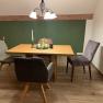 A dining table with four chairs in a room with a green accent wall and wooden floor.