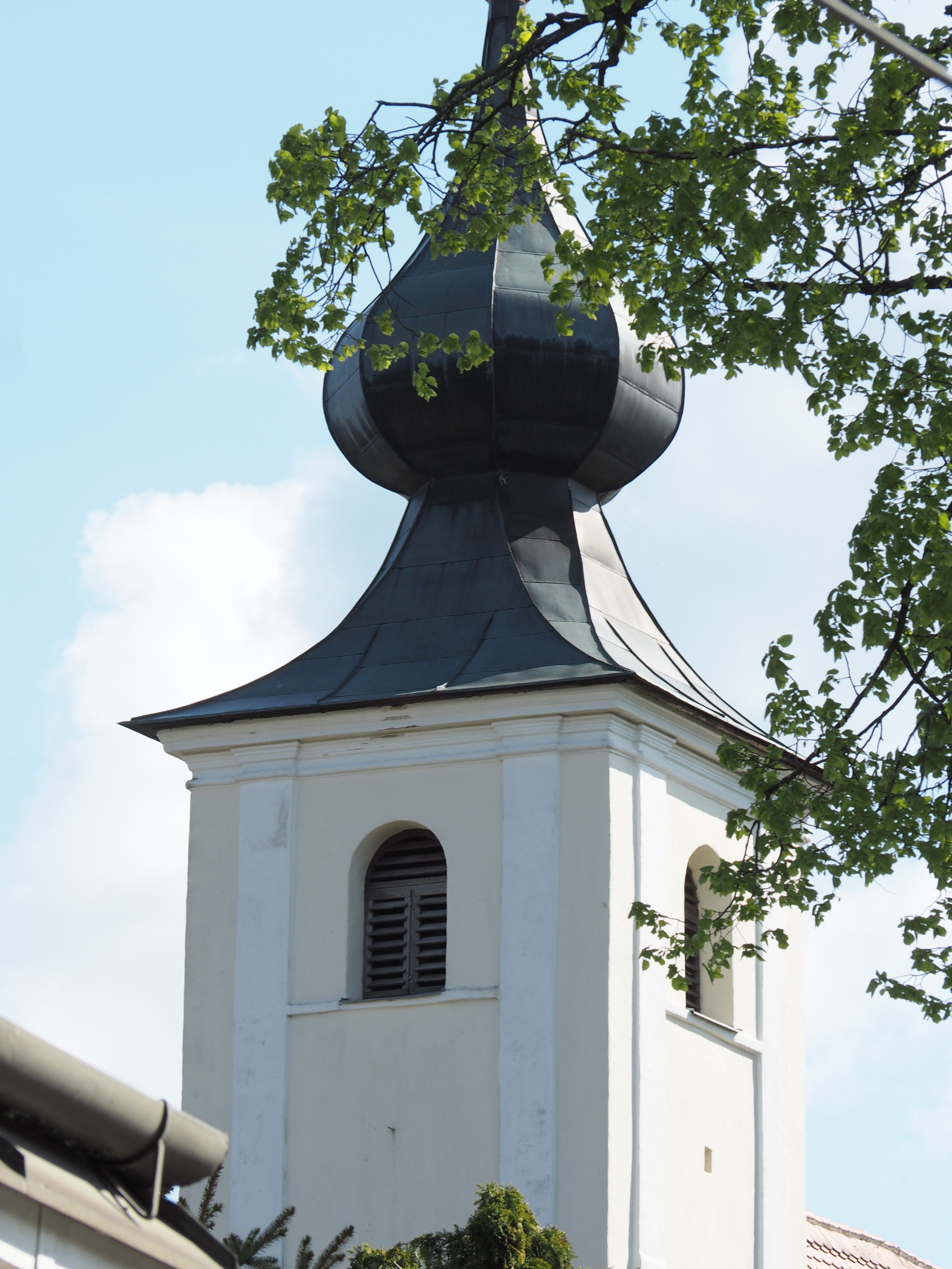 Church tower with onion dome and green leaves in the foreground.