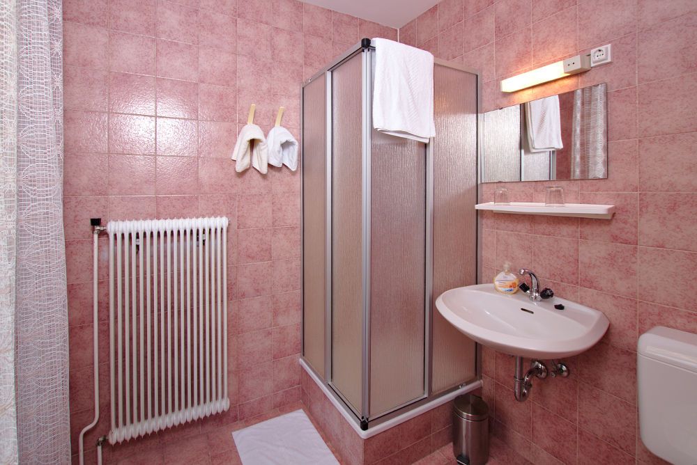 Bathroom with pink tiles, shower cubicle, washbasin and radiator.