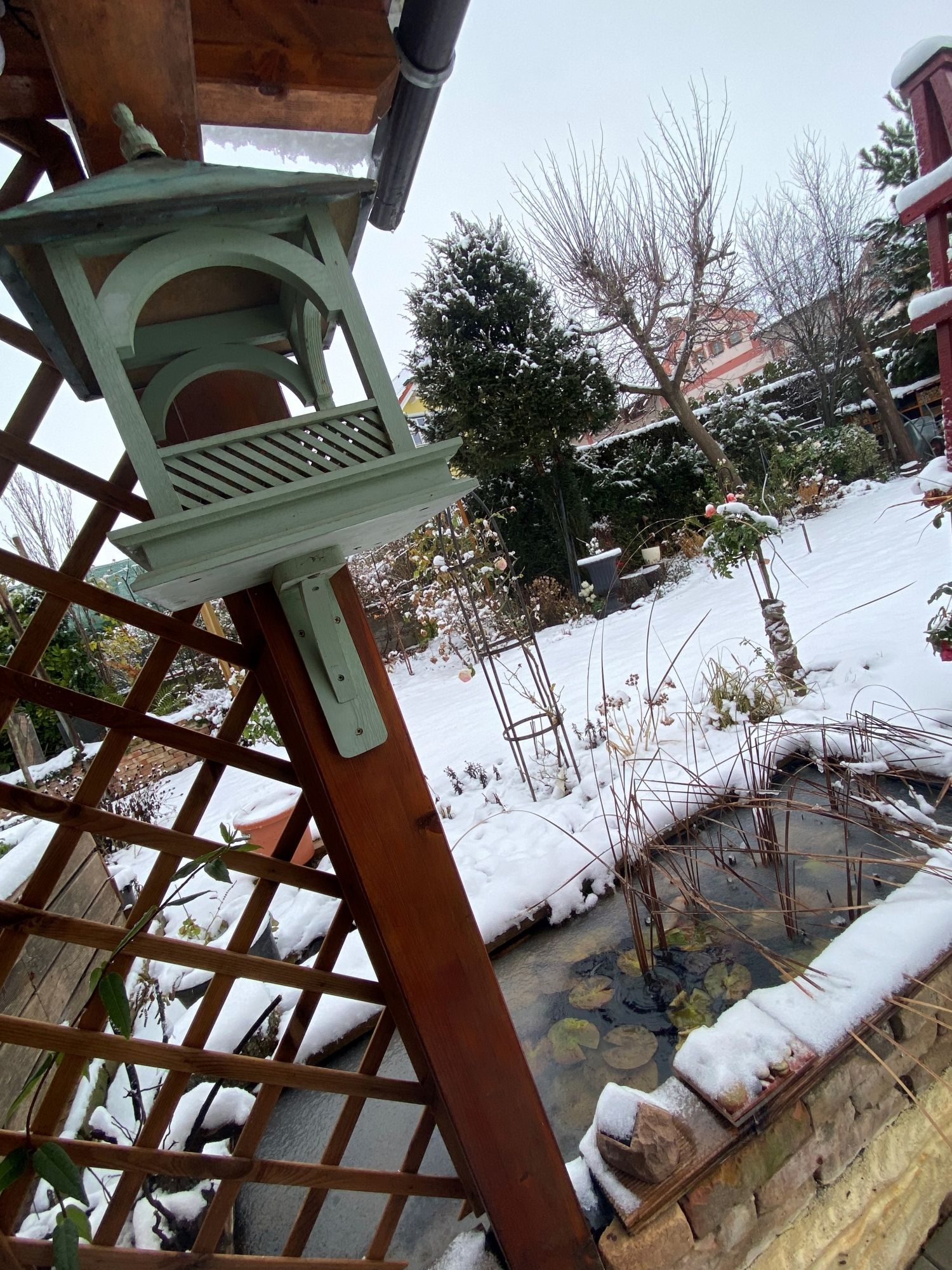 Snow-covered garden with bird house and pond.