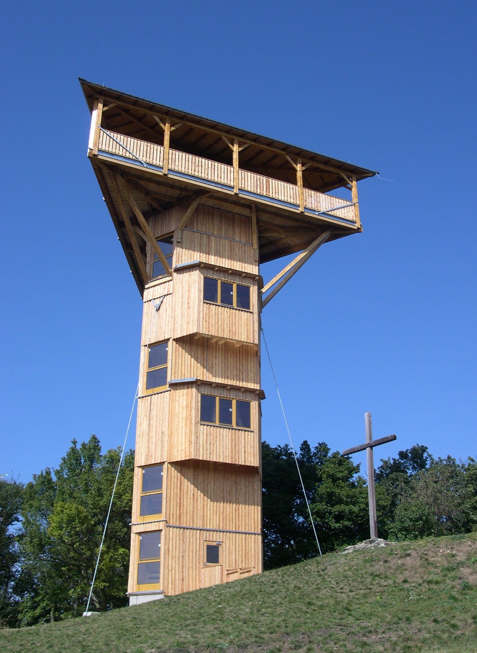 Wooden tower Buchbergwarte with cross next to it, blue sky.