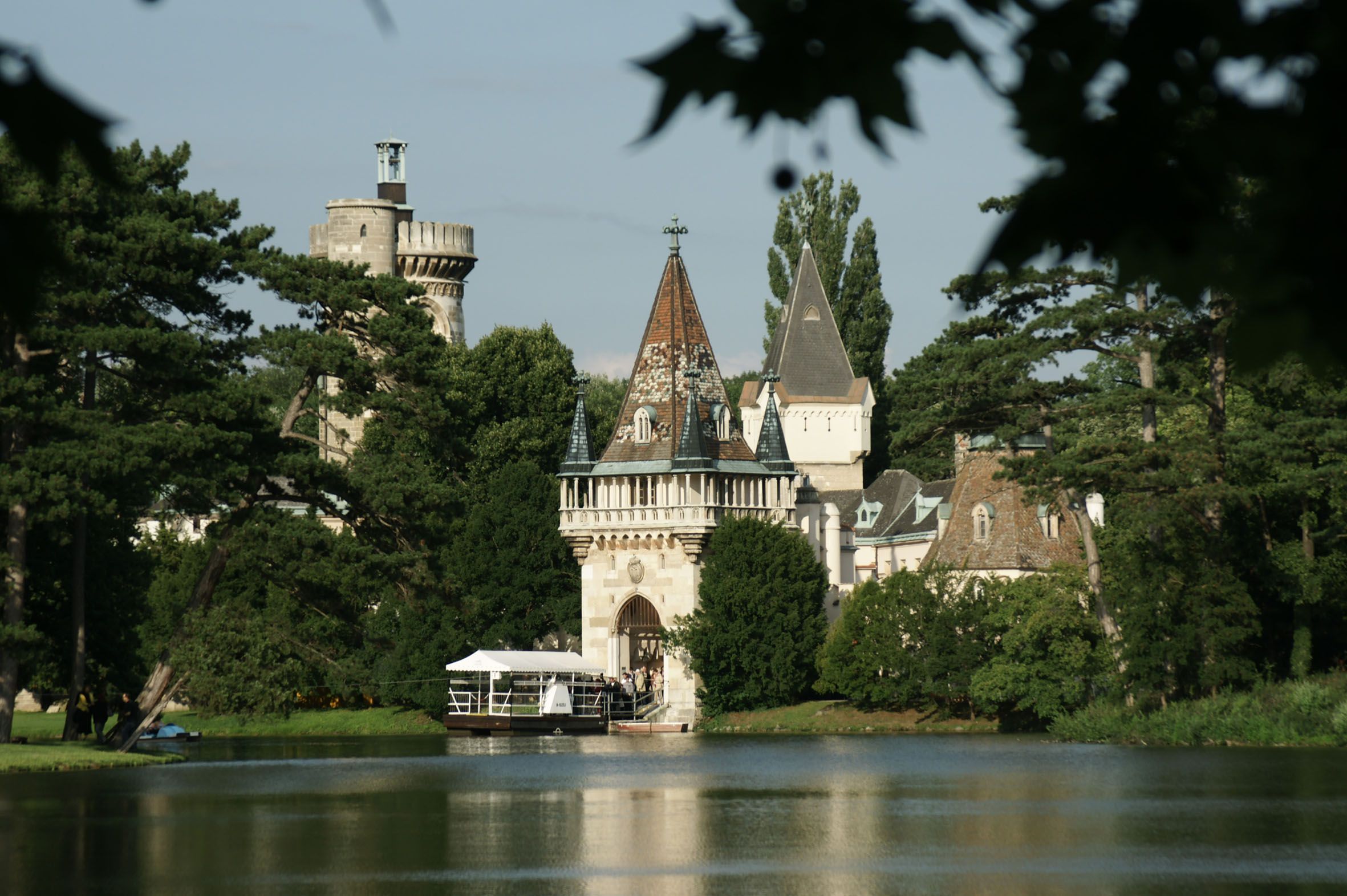 Laxenburg Castle with towers and trees on the lakeshore.