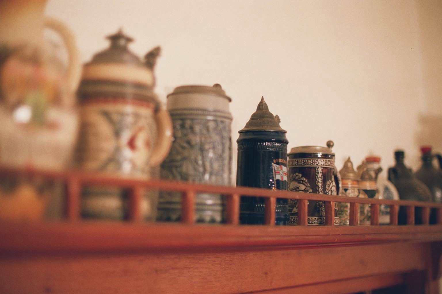 A collection of beer mugs on a wooden shelf, blurred in the foreground.