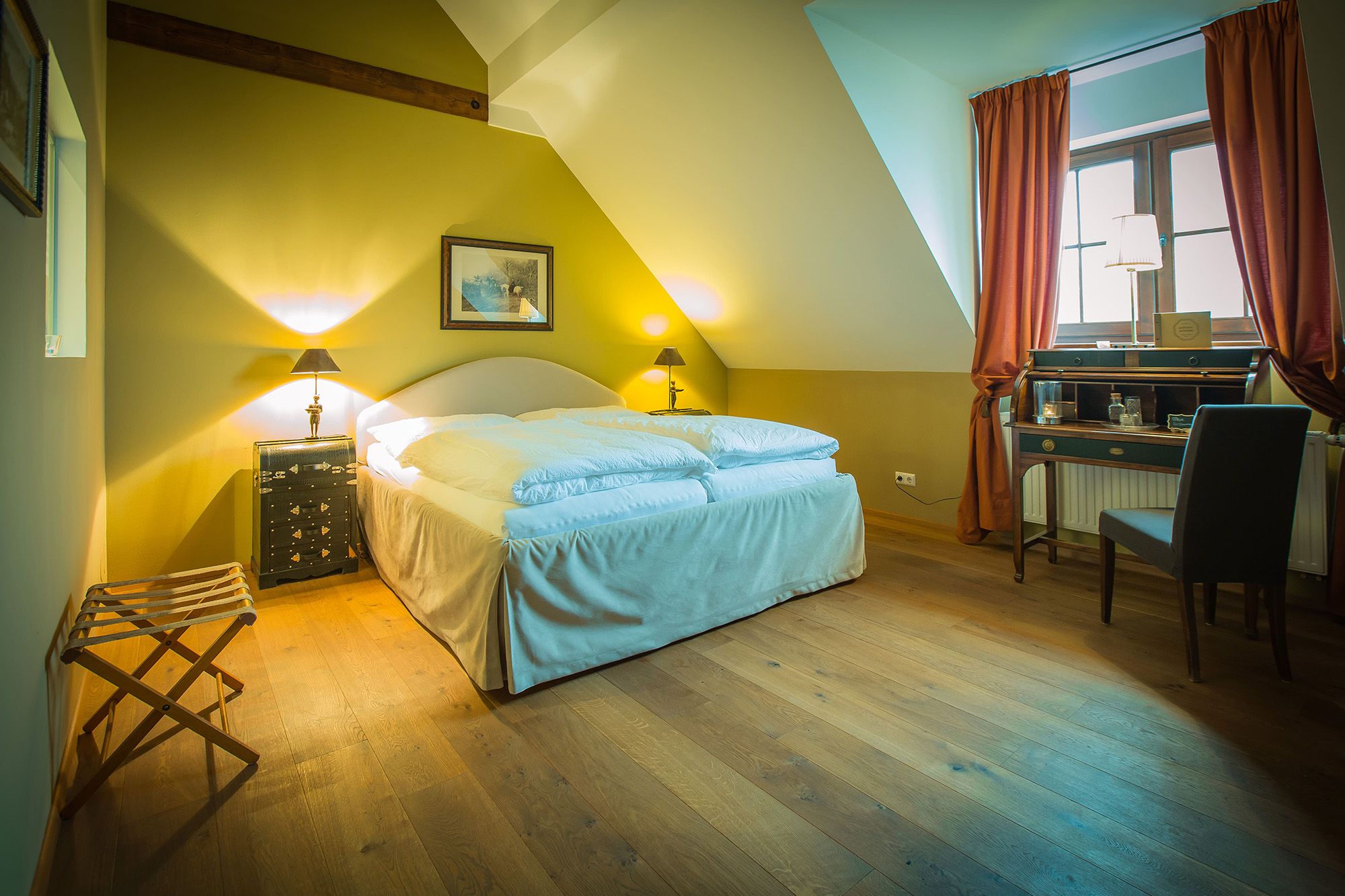 Cozy double room with wooden floor, double bed, desk and window with curtains.