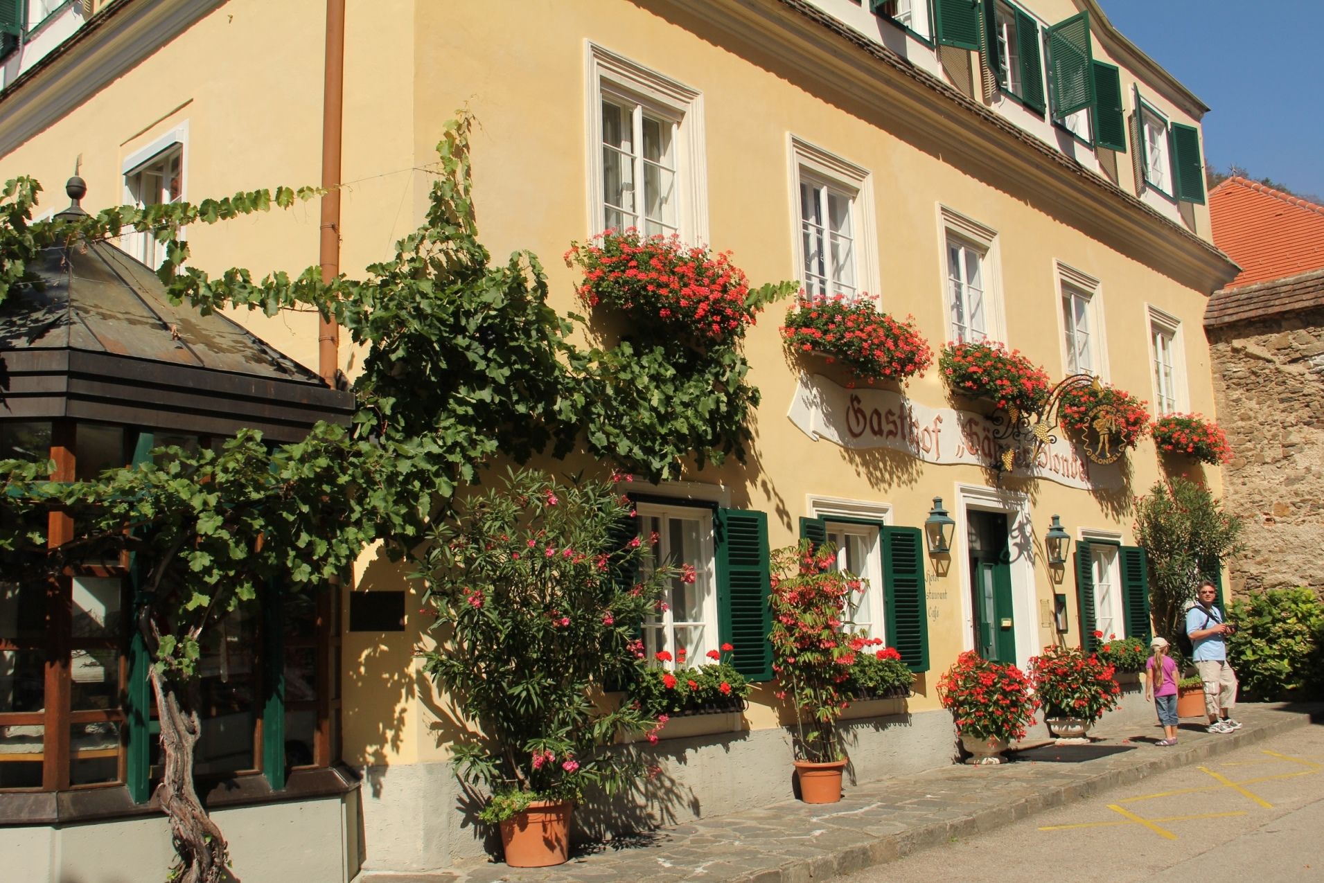A traditional inn with a yellow façade, green shutters and flower boxes in bloom.