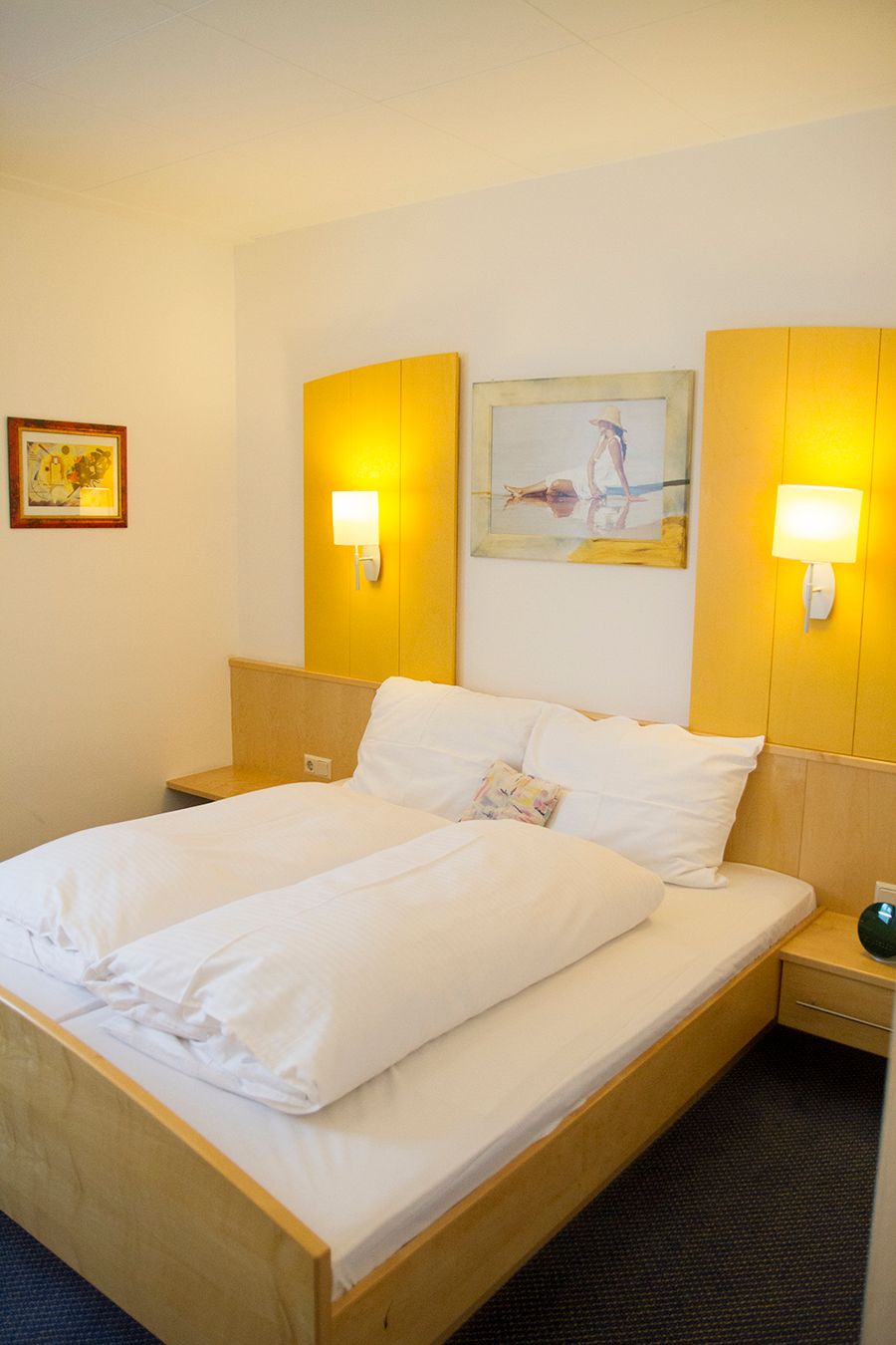 A cozy double room with a large bed, two wall lamps and two pictures on the wall.
