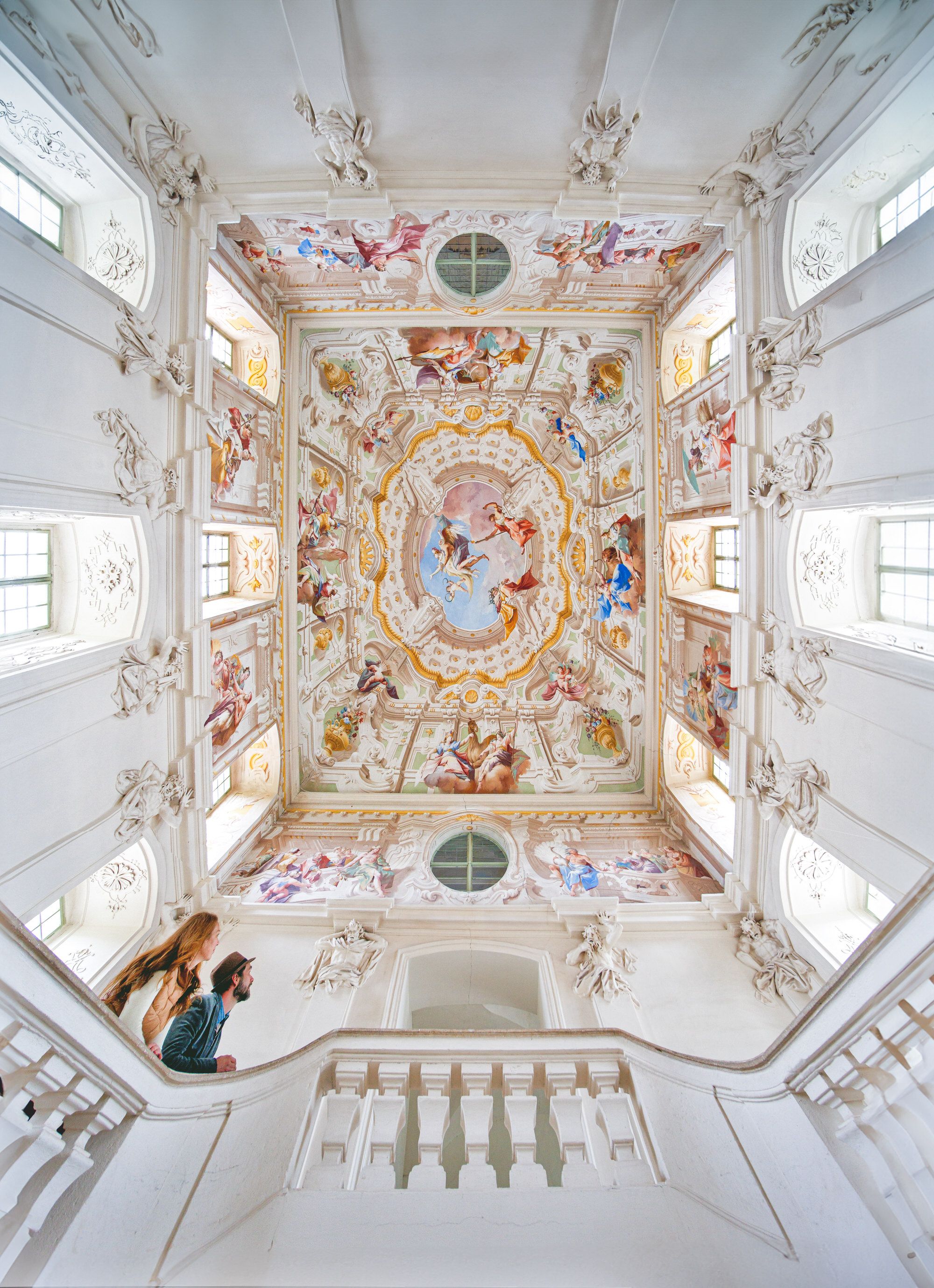 Two people look at the artistically painted ceiling of a baroque staircase in Altenburg Abbey.