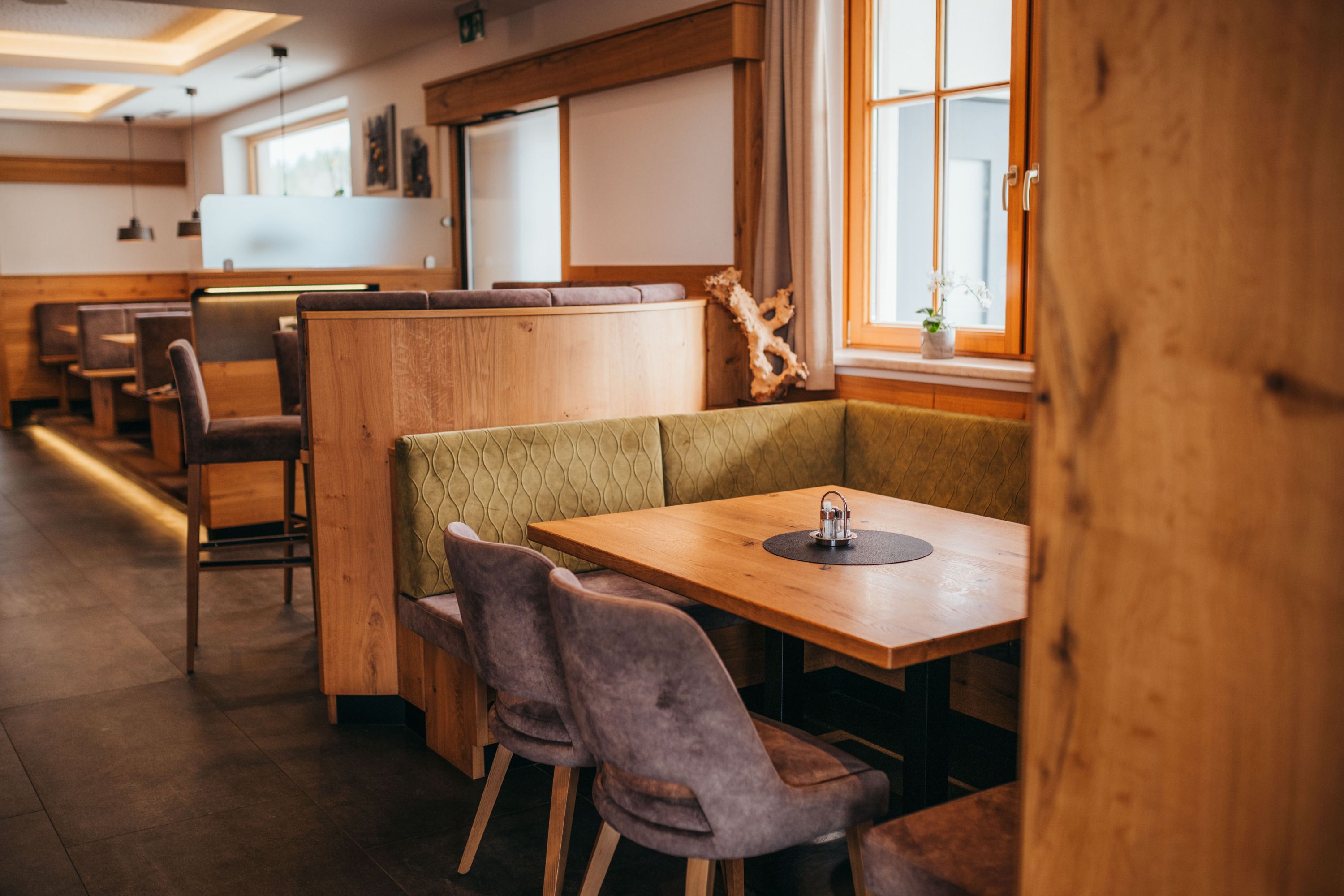 Cozy dining room with wooden furniture and upholstered benches, windows with curtains, table with salt and pepper shakers.