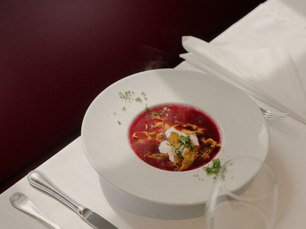 A plate of beetroot soup, garnished with cream and herbs, on a laid table.