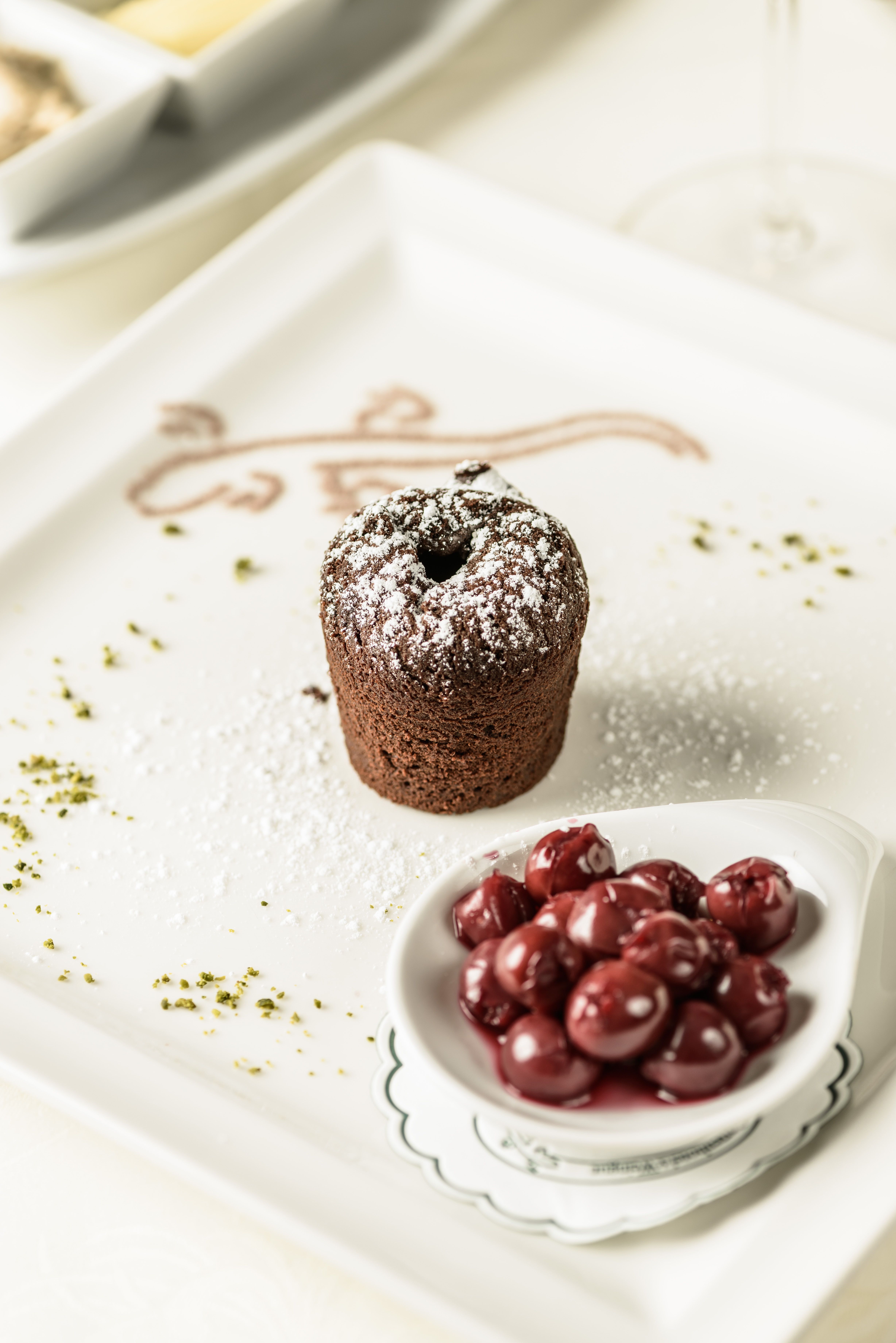 A chocolate cake with powdered sugar and cherries on a plate.